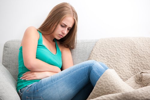 Young woman on a sofa holding her stomach in discomfort