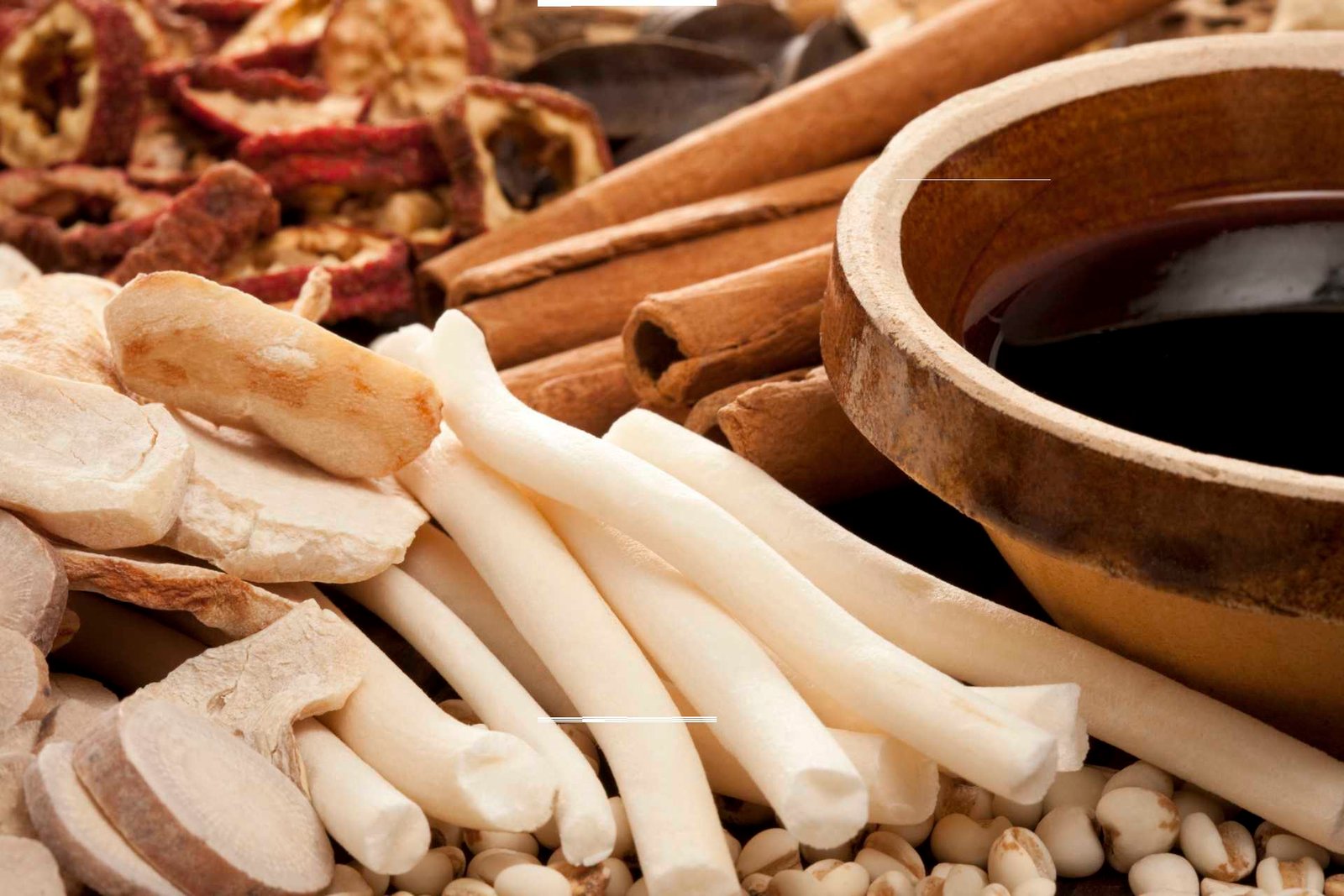 Dried Chinese herbs and roots beside a bowl of herbal tea