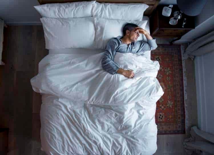 Man lying in bed holding his head