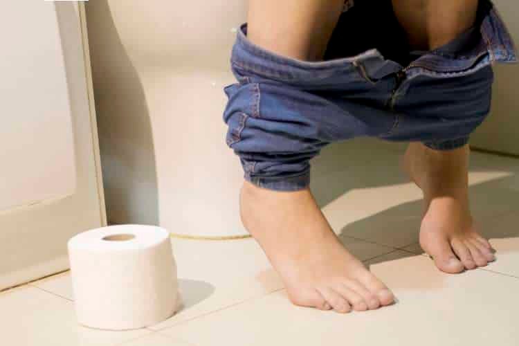 Person on a toilet with a roll of toilet paper nearby