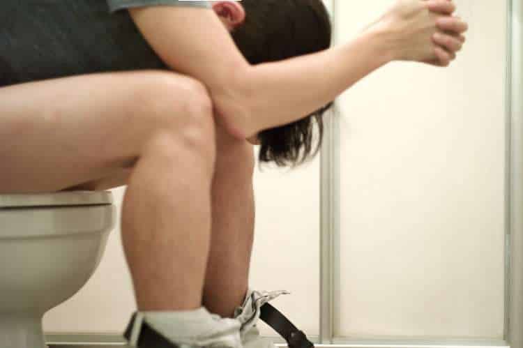 Person sitting on a toilet, bent forward