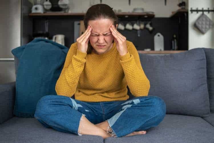 Woman sitting on a sofa holding her temples