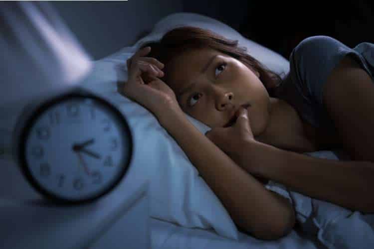 Woman awake in bed beside an alarm clock at night