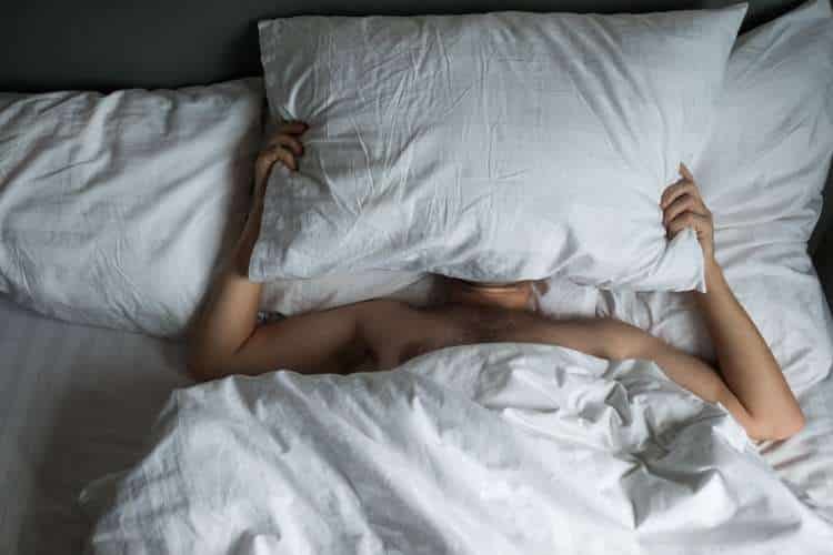 Person hiding under a pillow in bed
