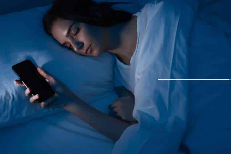 Woman in bed looking at her phone in the dark