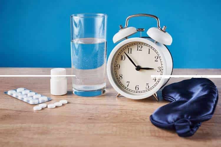 Alarm clock, glass of water, pills and a sleep mask on a table