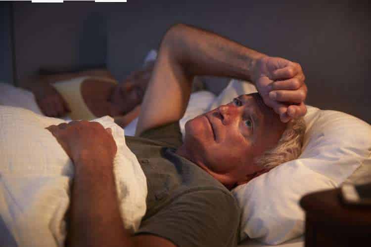 Older man awake in bed with a hand on his forehead