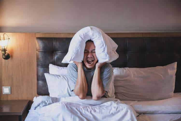 Woman in bed pulling a pillow over her ears