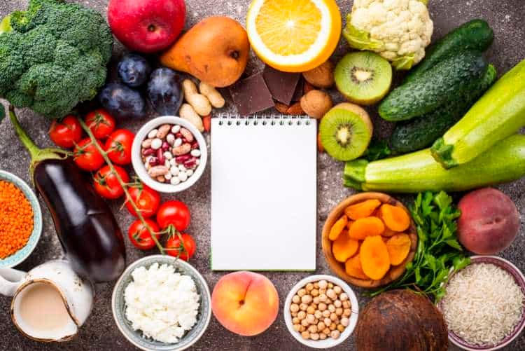 Fresh vegetables, fruit, grains and a notepad on a table