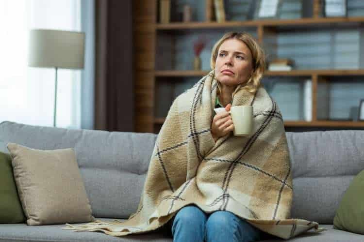 Woman on a sofa wrapped in a blanket, holding a mug