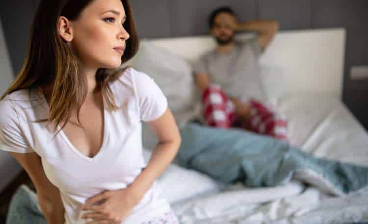 Woman in bed holding her stomach while her partner rests behind her