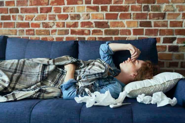 Man lying on a sofa with tissues, holding his forehead